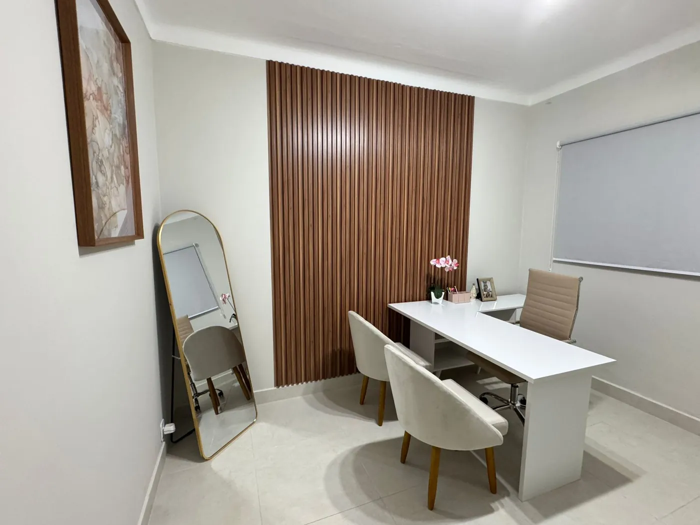 Sala de atendimento do consultório, com mesa branca, poltronas e painel de madeira